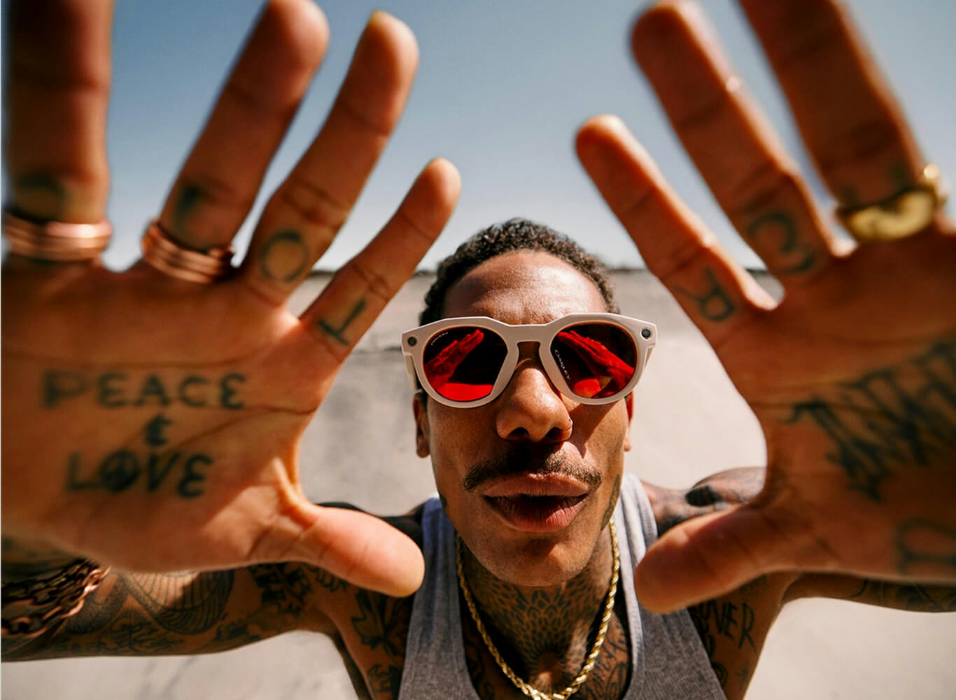 Een man met een Oakley Meta-zonnebril houdt zijn handen omhoog naar de camera, met tatoeages op zijn vingers met de tekst "PEACE" en "LOVE"
