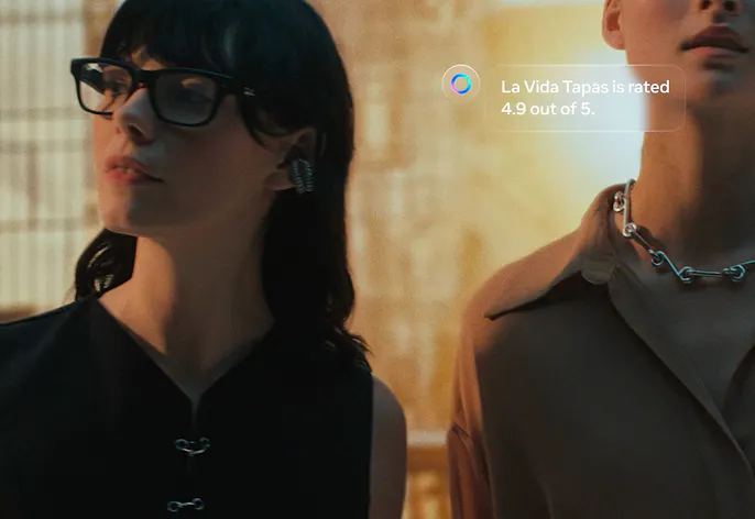 Dos personas llevan gafas inteligentes Ray-Ban Meta mientras una valoración aparece superpuesta en pantalla.
