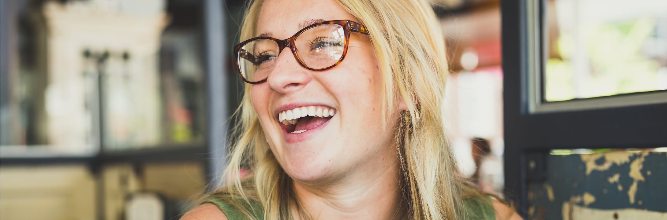 Head and shoulders of smiling woman with long blonde hair wearing a green top and tortoiseshell glasses.