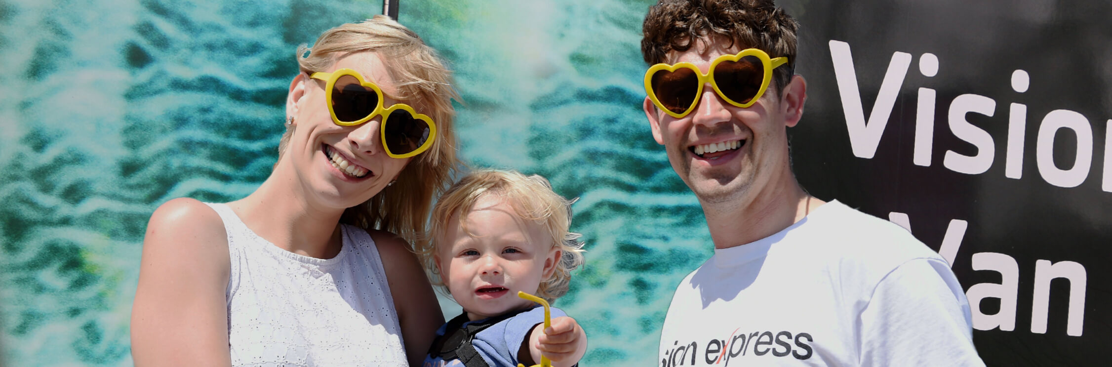 Young man, woman and child wearing yellow heart-shaped sunglasses outside the Vision Express Vision Van.